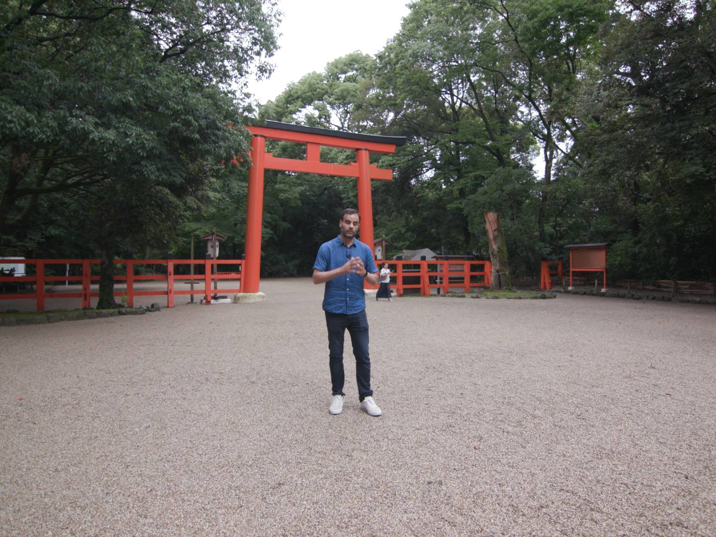 画像: 赤い鳥居の前に立つ人物と周囲の緑豊かな自然の風景が特徴の神社境内です。観光名所、日本文化、京都、神社、新緑がキーワードです。
