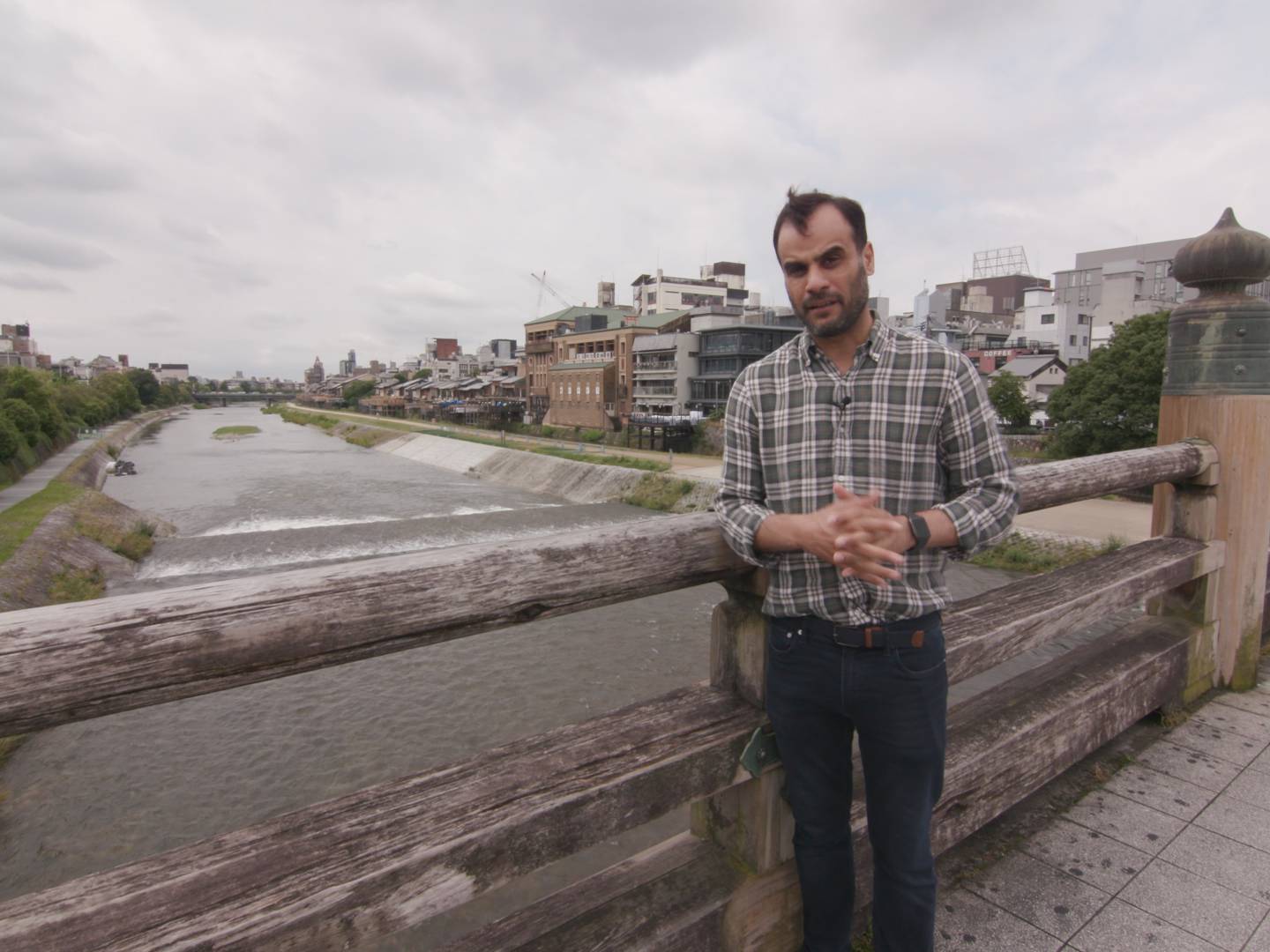画像: 鴨川に架かる四条大橋で立つ男性。背景には鴨川が流れており、京都市の街並みが広がる。風景、旅行、京都観光、橋