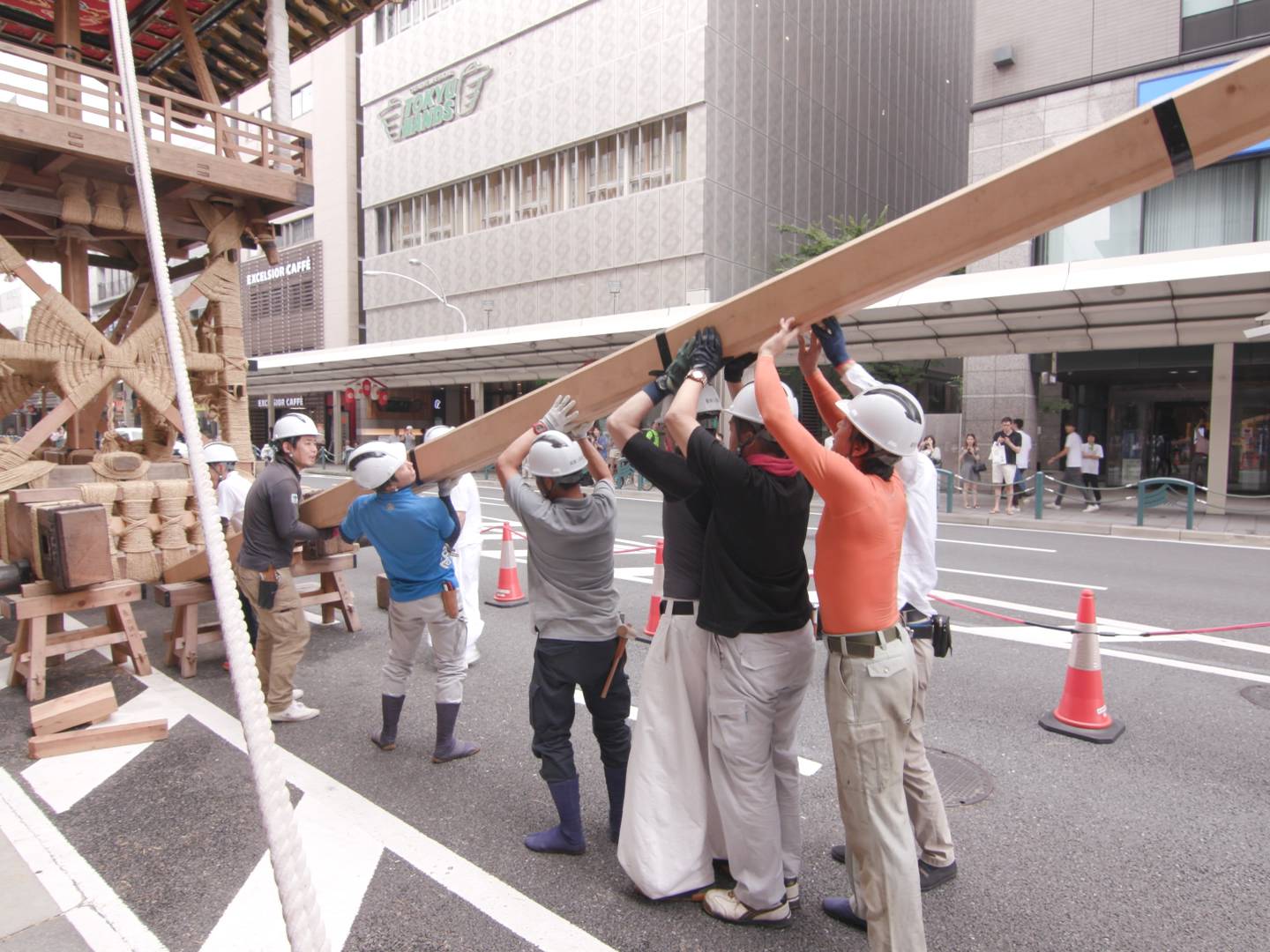 画像: 画像は、京都の祭りである祇園祭の準備中の様子を示しています。作業員たちが、山鉾の組み立て作業を進めています。背景には、街
