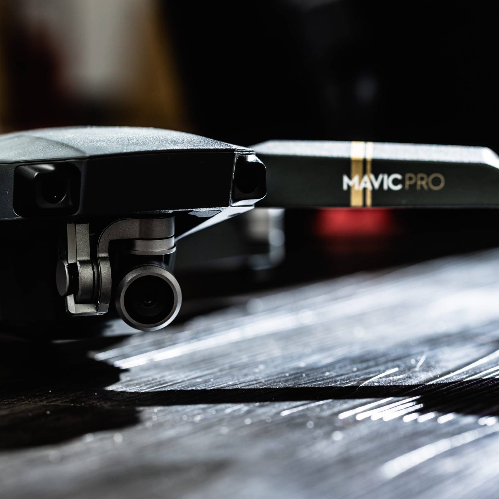 画像: 黒いテーブルの上に置かれたドローン「Mavic Pro」のクローズアップ画像。カメラとプロペラが見え、シンプルで洗練されたデザインが特徴的。